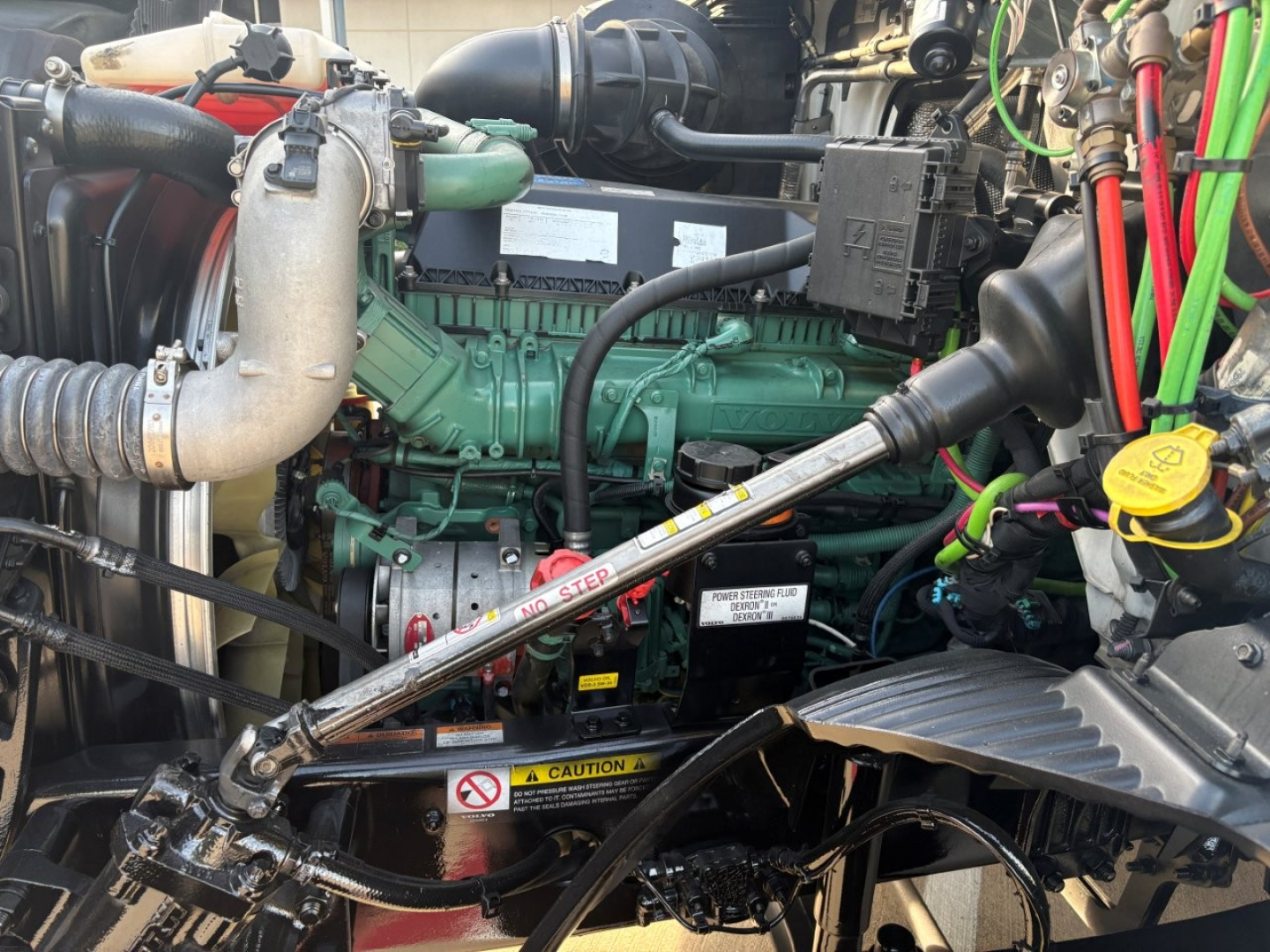 Volvo VNR64T300 engine bay showing green Volvo engine with black hoses, silver exhaust, and various colored wires and components.