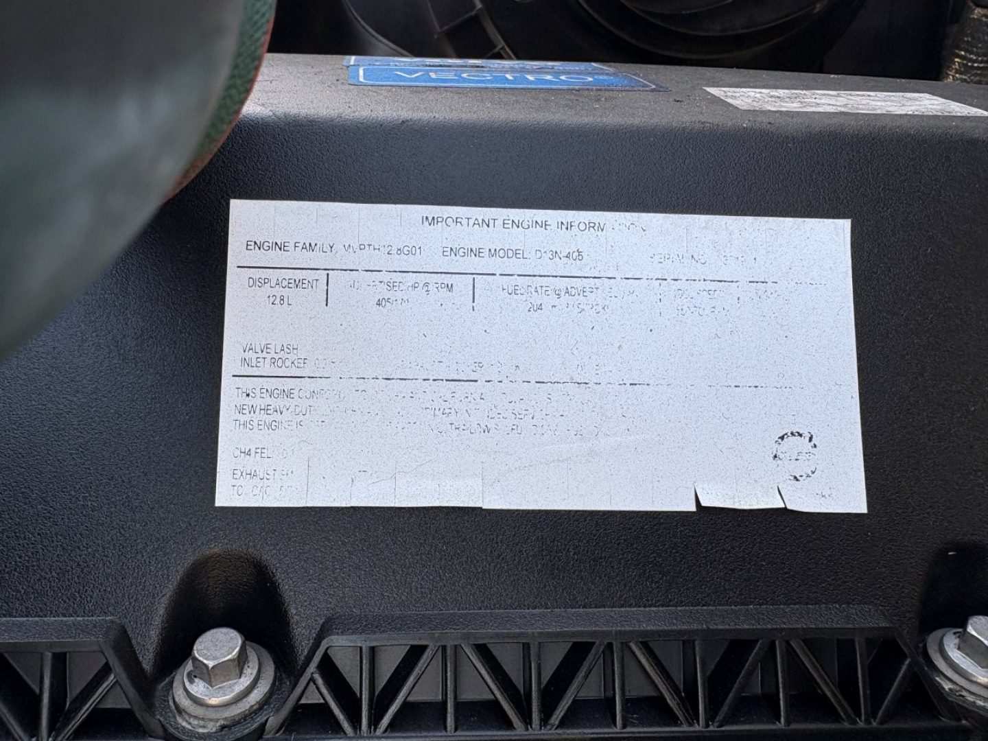 Label on engine bay with engine family and serial information plate; sticker text is faint but shows ENGINE FAMILY and important engine information, mounted on a black plastic panel.