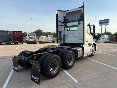 Volvo VNR64T300 daycab truck rear view showing tandem dual rear axles and white sleeper cab, with Volvo dealership in background