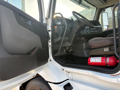 Volvo VNR64T300 interior cab view with steering wheel, dashboard, and open door. Fire extinguisher mounted on floor area near passenger side. VIN plate not visible.