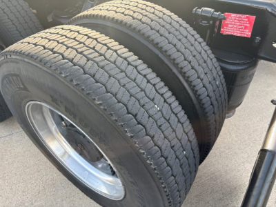 Twin rear wheels of a Volvo VNR truck showing rubber tires and chrome rims with a red warning label on the air suspension; part of the rear axle assembly.