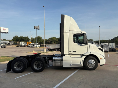 Volvo VNR64T300 daycab tractor shown in side profile with sleeper, cab high roof, diesel fuel tanks, and tri-axle rear wheels in a parking lot.