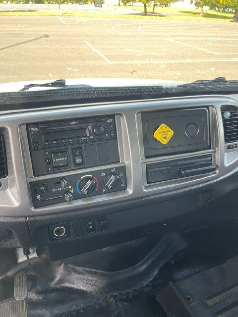 Dashboard of a 2017 Hino 268 with steering wheel on left, center console, climate controls, radio, and a yellow diamond hazard placard on the passenger side dash.