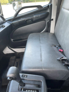 Seat belt and front passenger seat in a 2017 Hino 268 cab interior with black vinyl bench seat, door panel, and gear shifter visible.