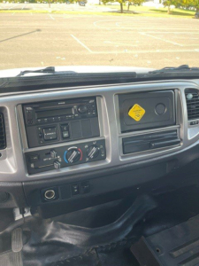 Dashboard of a 2017 Hino 268 with steering wheel on left, center console, climate controls, radio, and a yellow diamond hazard placard on the passenger side dash.