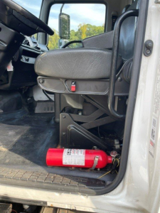 Cab interior of a 2017 Hino 268 truck showing driver seat, steering wheel, and a red fire extinguisher mounted near the door sill.