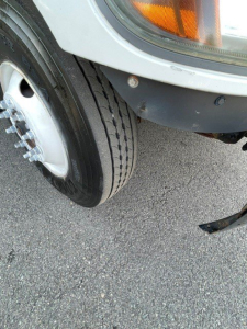 Front wheel and fender area of a 2017 Hino 268 box truck showing tire and bumper with a small bolt and reflector.