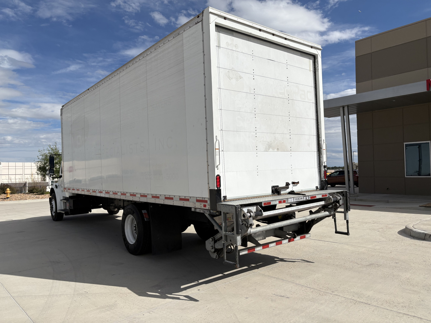 Freightliner M2-106 rear/side view showing a large white box truck trailer with rear liftgate and bumper undercarriage.