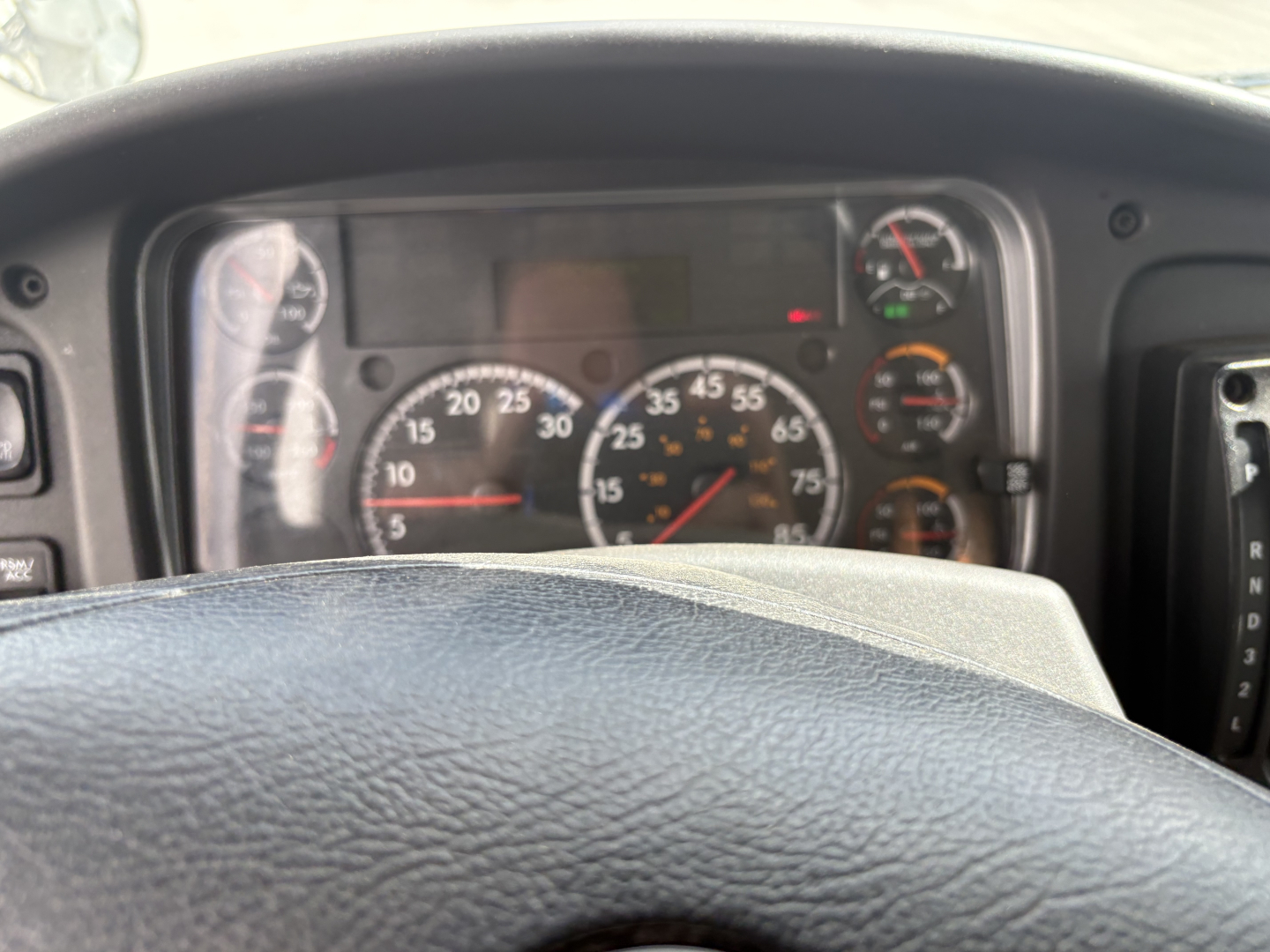 Truck interior dashboard of a Freightliner M2-106 showing speedometer and gauge cluster behind steering wheel.