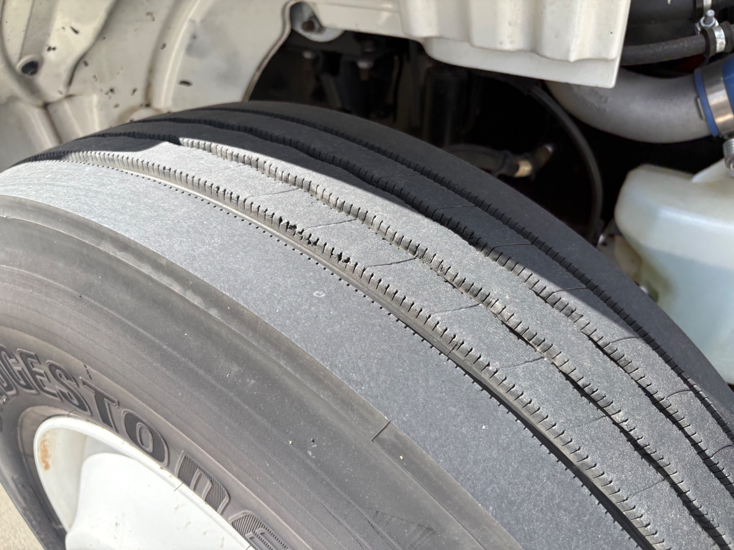 Front left wheel and fender of a Freightliner M2-106 showing Bridgestone or generic dual tread tire and parts of wheel well and engine bay.