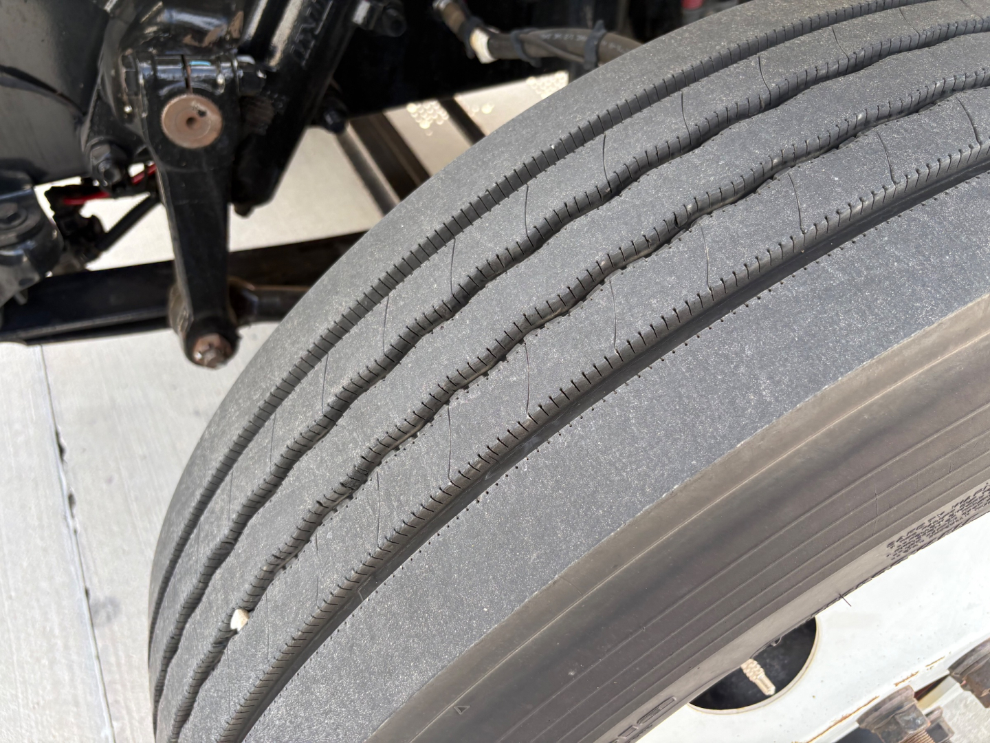 Freightliner M2-106 wheel and front tire close-up showing dual tread pattern on the front axle, with suspension components and frame visible in background.