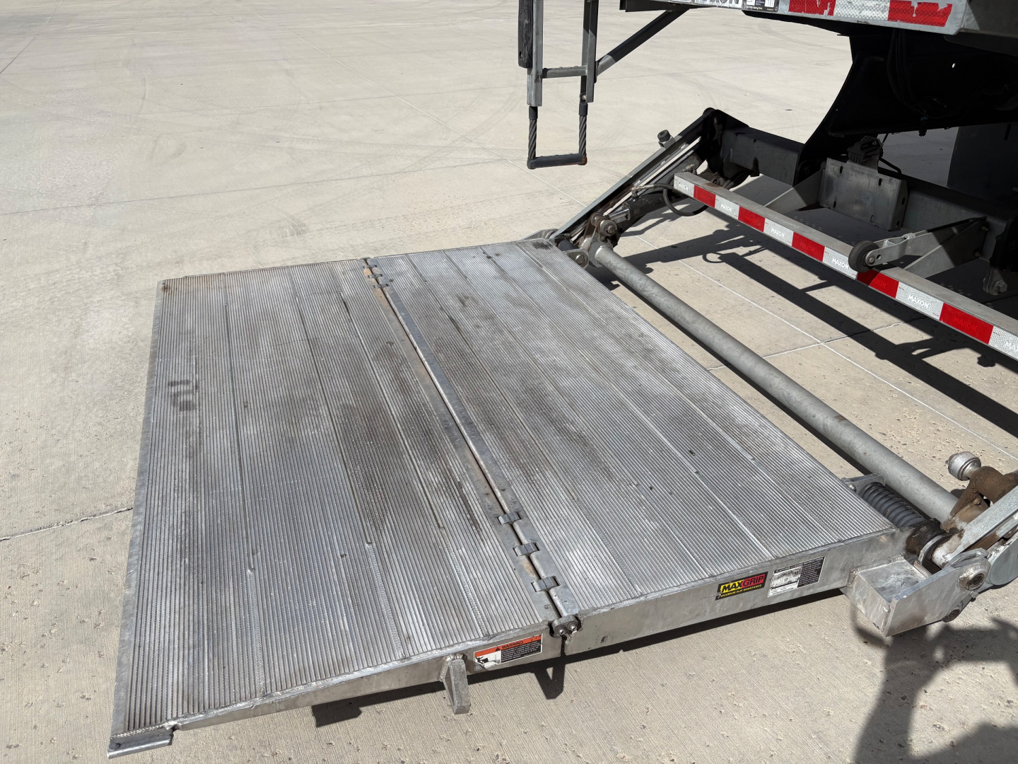 Aluminum loading ramp/platform extended from a Freightliner M2-106 truck showing surface ridges and hinge area.