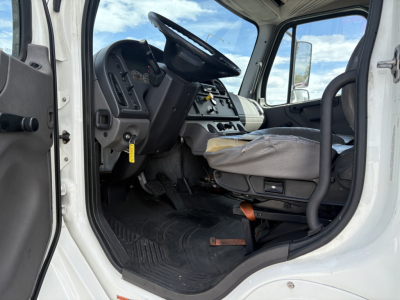 Cab interior of a Freightliner M2-106 with steering wheel, dashboard, and driver's seat visible from open door.