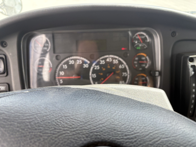 Truck interior dashboard of a Freightliner M2-106 showing speedometer and gauge cluster behind steering wheel.