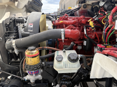 Freightliner M2-106 engine bay showing coolant reservoir, hydraulic lines, red engine components, and black radiator hose.