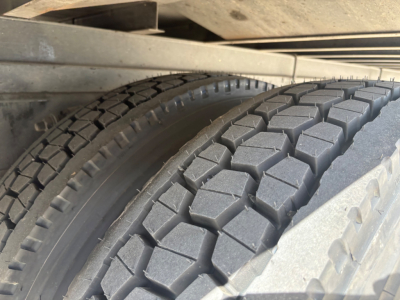 Freightliner M2-106 wheel and dual tires with tread pattern visible under truck frame; metal suspension components and frame rail above.