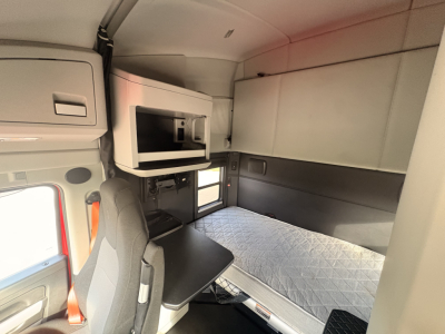 Kenworth T680 sleeper cab interior with bed and workspace, cabin storage above, and window visible.