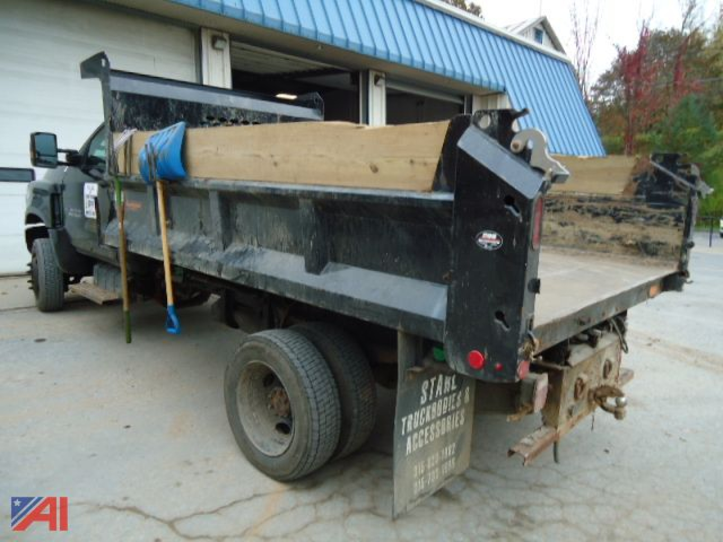 Dump truck rear view showing V-plow mount and wooden dump bed with taillights, wheel, and dirt inlay. Visible stickers and equipment hitch.