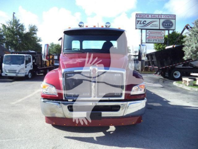 Front view of a red Kenworth truck in a dealership lot with a large chrome grille and bumper; a sign in background reads TLC Truck Sales Center and ETV, with other trucks parked nearby.
