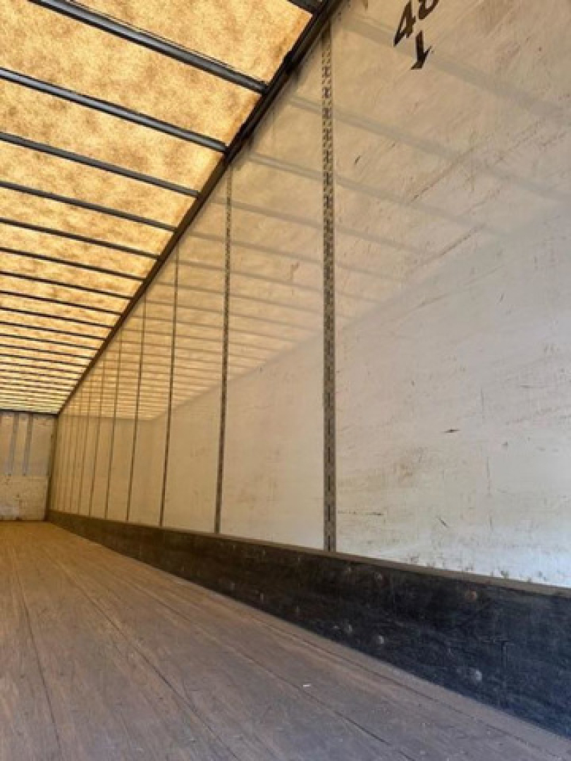 Interior of a trailer with wooden floor and white side walls; top edge shows metal framing and translucent roof panels