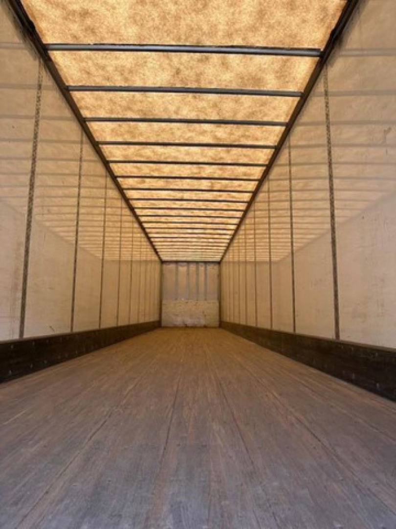 Trailer interior showing empty cargo van with wooden floor, side walls, and roof ribs; no visible text or labels inside.