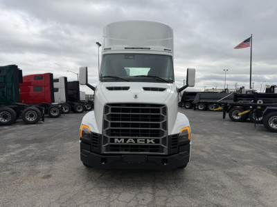 Front view of a white Mack AN64T truck with large grille, headlights, and 'MACK' emblem; parking lot with other trucks in background.