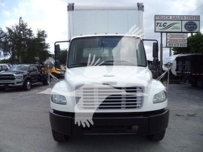 Box truck front view showing Freightliner logo, grille, windshield, headlights. There is signage in background with ‘TRUCK SALES CENTER’ and phone numbers.