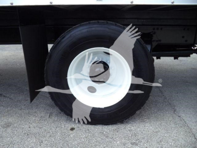 Wheel and tire of a Freightliner M2 106 truck showing a white steel wheel and black tire under a flatbed, with chassis and mudguard visible.