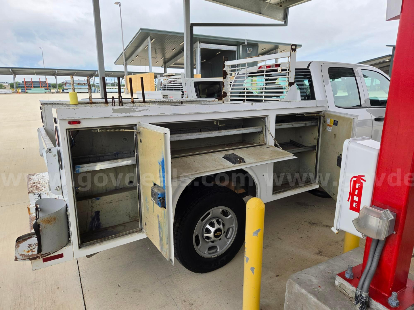 Service/utility truck body showing open compartments with shelves and tool storage, Silverado 2500 utility bed and spare tire visible.