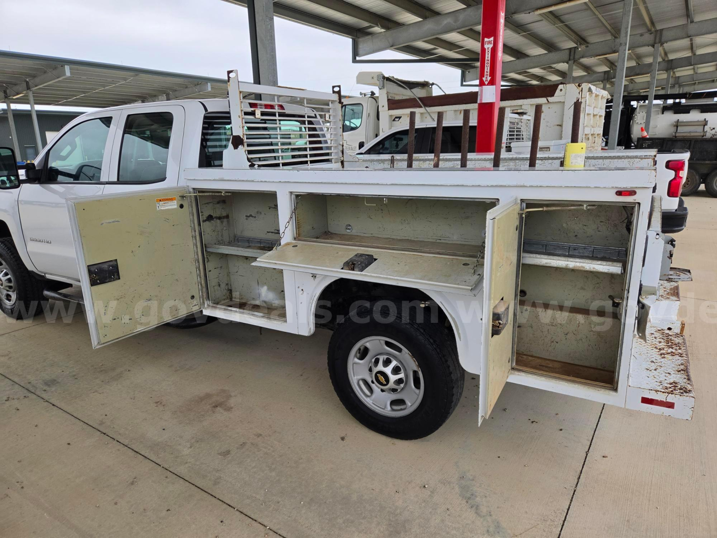Front side of a white utility service truck with open side compartments showing storage bins and metal shelving.