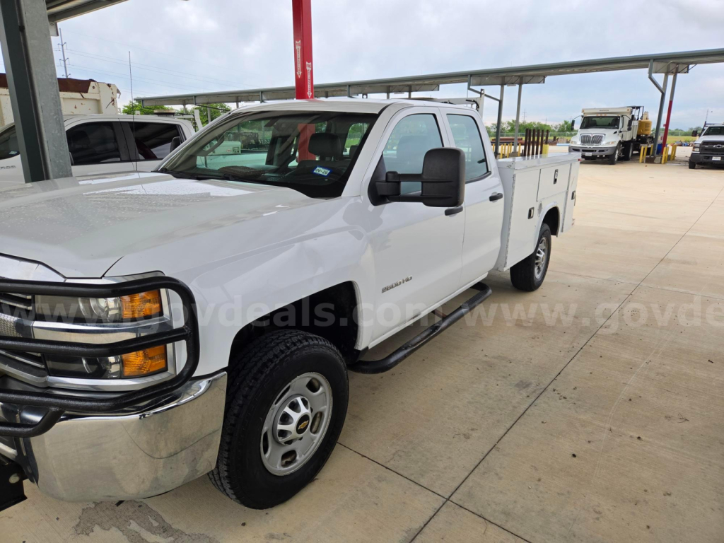 White Chevrolet Silverado 2500HD service/utility pickup truck with extended cab and utility bed, front chrome bumper, black mirrors, black running boards, dealership lot