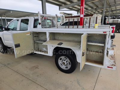 Front side of a white utility service truck with open side compartments showing storage bins and metal shelving.