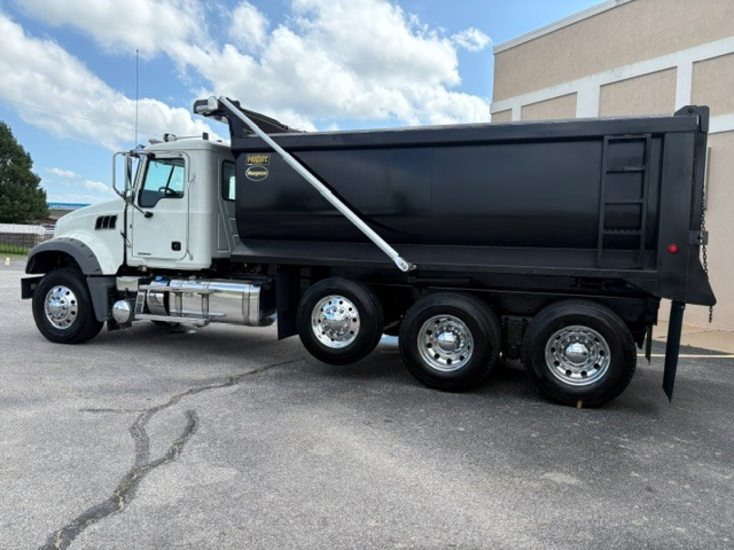 Dump truck side view showing white cab and black dump bed with three axles and chrome wheels, Mack GR84F model.