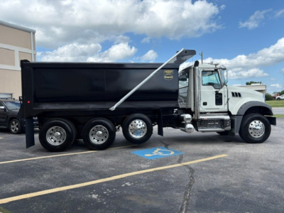 Dump truck side view showing Mack GR84F with black dumping bed, white cab, chrome wheels, and hydraulic hoist.