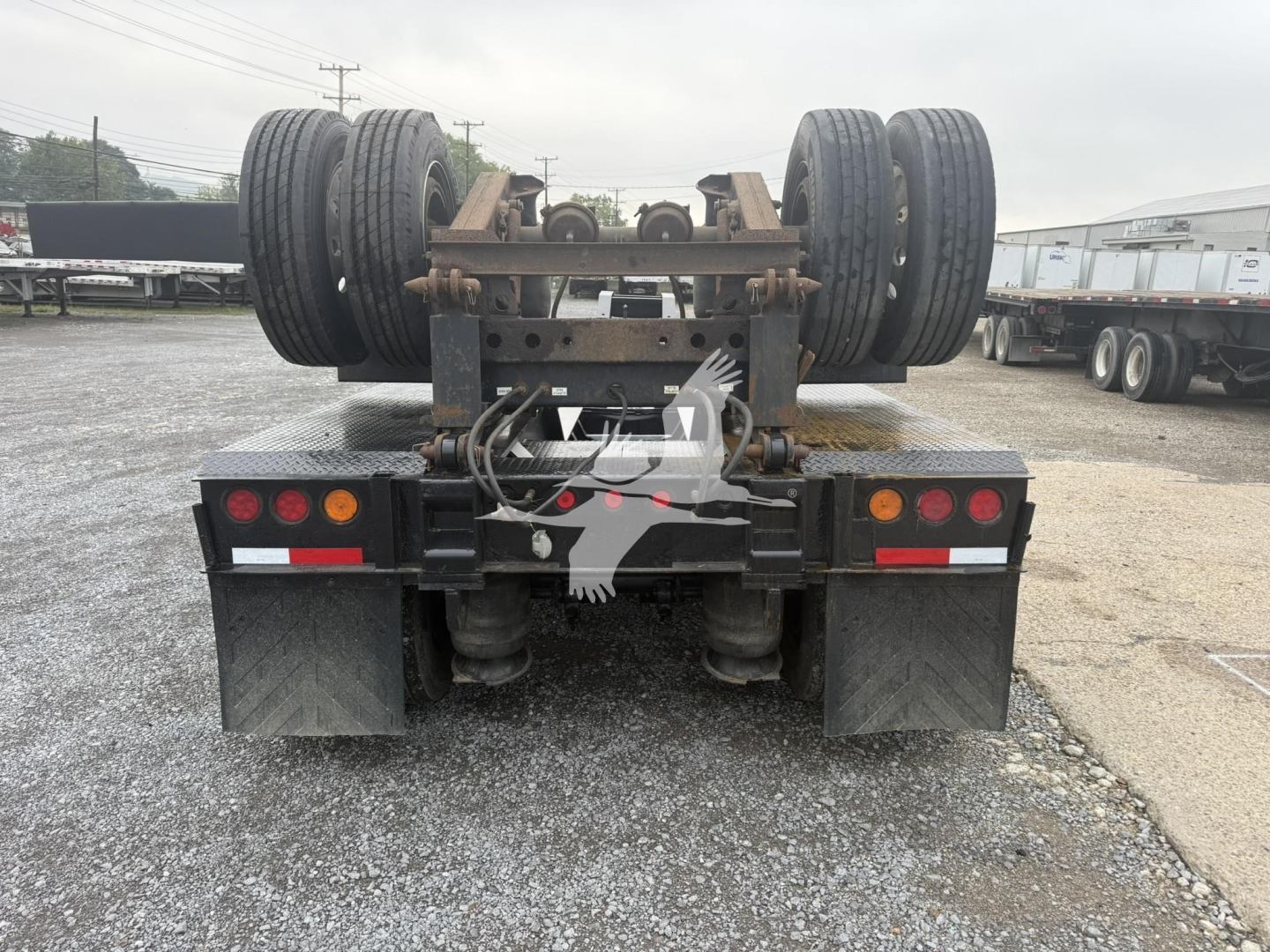 Rear view of a used lowboy trailer showing tandem axles and tires, with suspension frame and mudflaps.