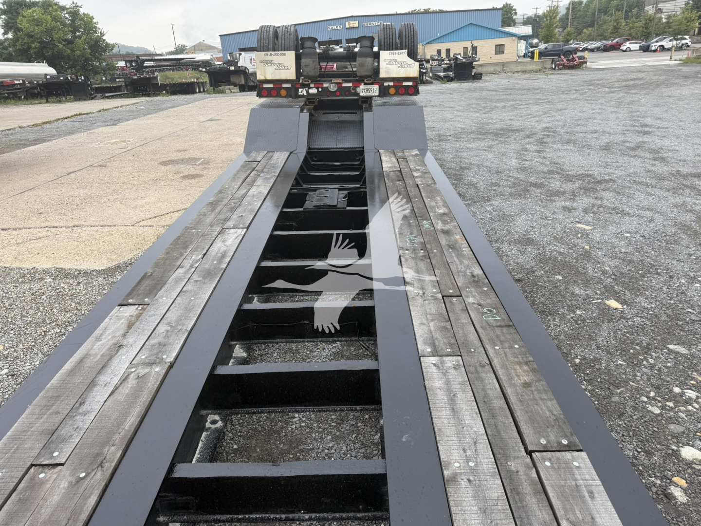 trailer bed of a lowboy trailer showing wooden deck sections and metal beams, viewed from front toward the cab area in a parking lot