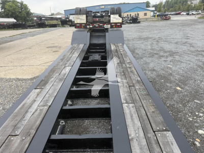  trailer bed of a lowboy trailer showing wooden deck sections and metal beams, viewed from front toward the cab area in a parking lot