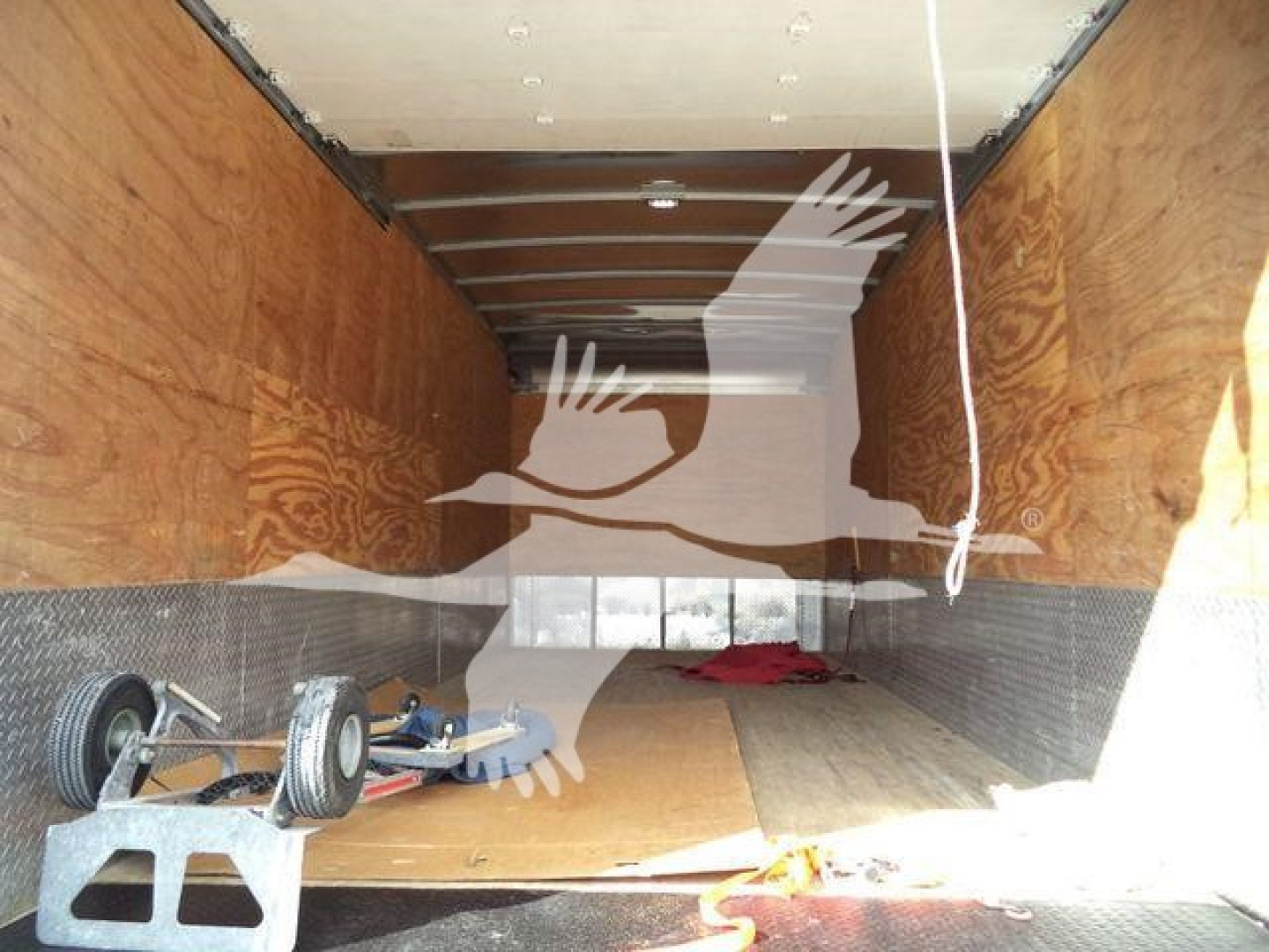 Isuzu NRR truck cargo area displaying wooden interior walls and a partially loaded trailer with a small wheel assembly and tools on the floor.