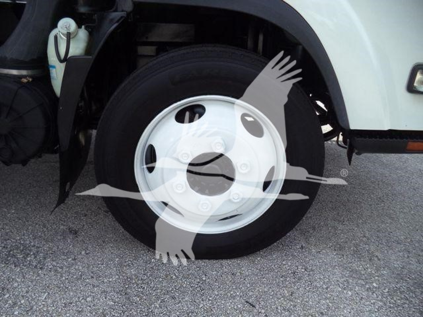 Isuzu NPR/NRR truck front wheel well showing steel wheel, tire, and part of fender with coolant reservoir visible