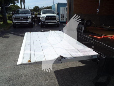 Isuzu NPRR flatbed truck bed platform with white metal deck extended from a trailer, parked outdoors with other trucks in background.