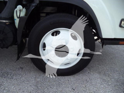 Isuzu NPR/NRR truck front wheel well showing steel wheel, tire, and part of fender with coolant reservoir visible