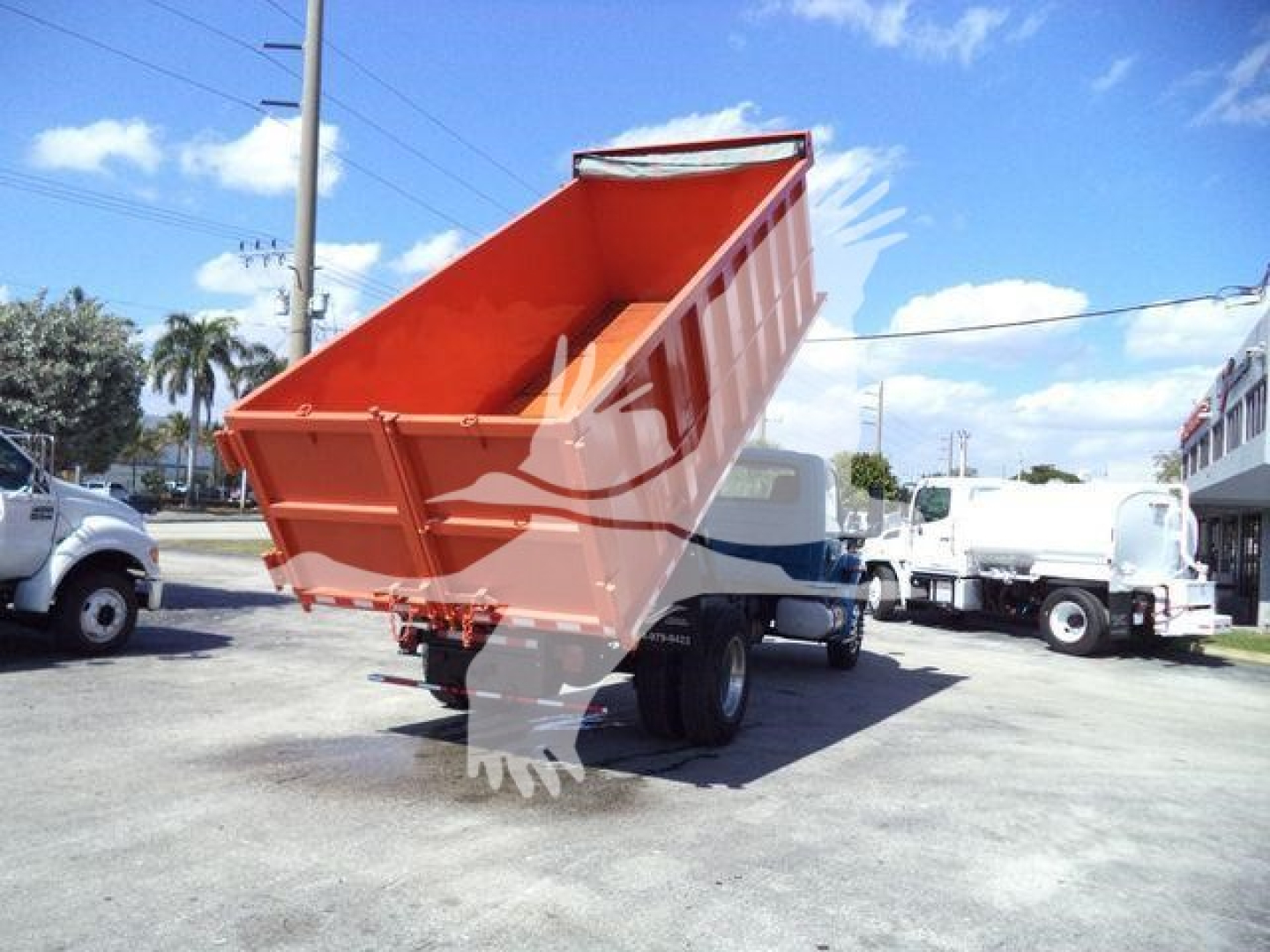 Dump truck bed raised at an angle showing orange dump bed on a white International MV chassis in a dealership lot.