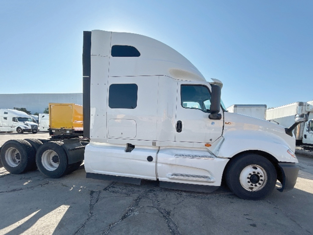 Truck cab of a 2022 International LT625 conventional sleeper tractor in white, side view with dual rear axles and revealed VIN sticker area visible.