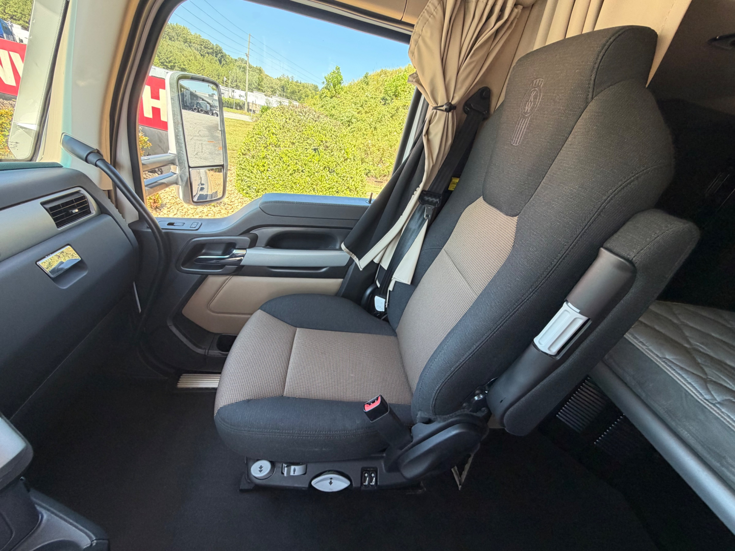 Cab interior of a Kenworth truck indicating driver and passenger seats with seat controls on the base and door panel visible.