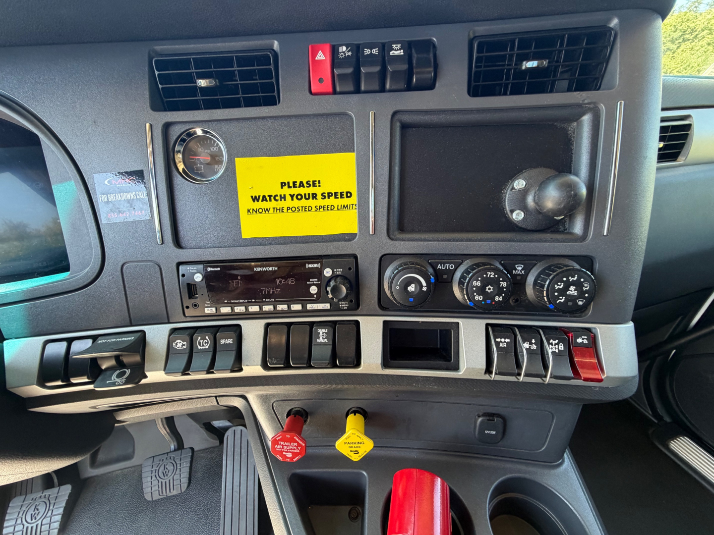 Truck dashboard with control switches, yellow warning sticker and various gauges. Visible text includes 'PLEASE WATCH YOUR SPEED', various switch labels, and a yellow key tag.