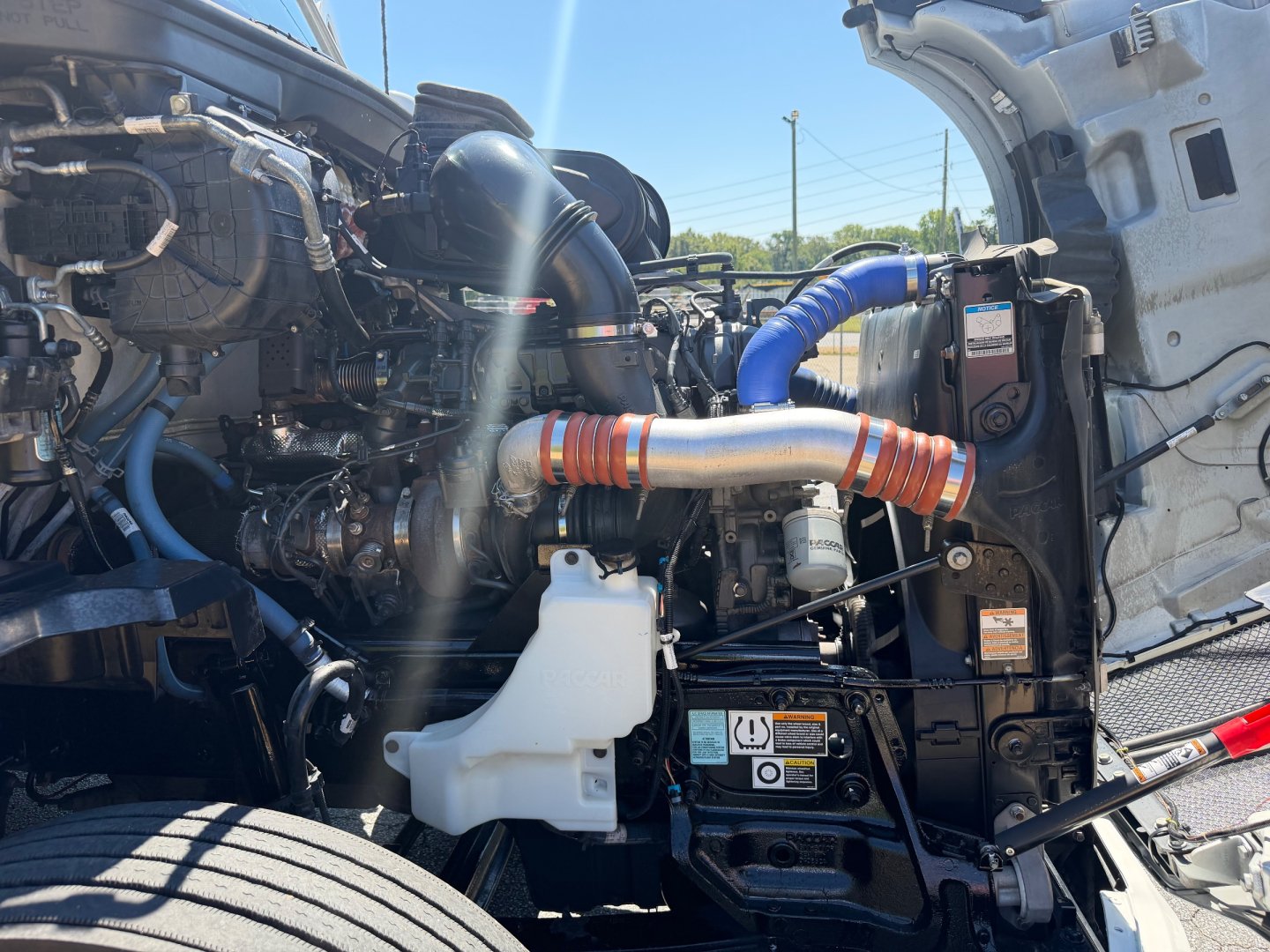 Kenworth T680 engine bay showing intake, turbo piping, coolant reservoir, and various hoses.
