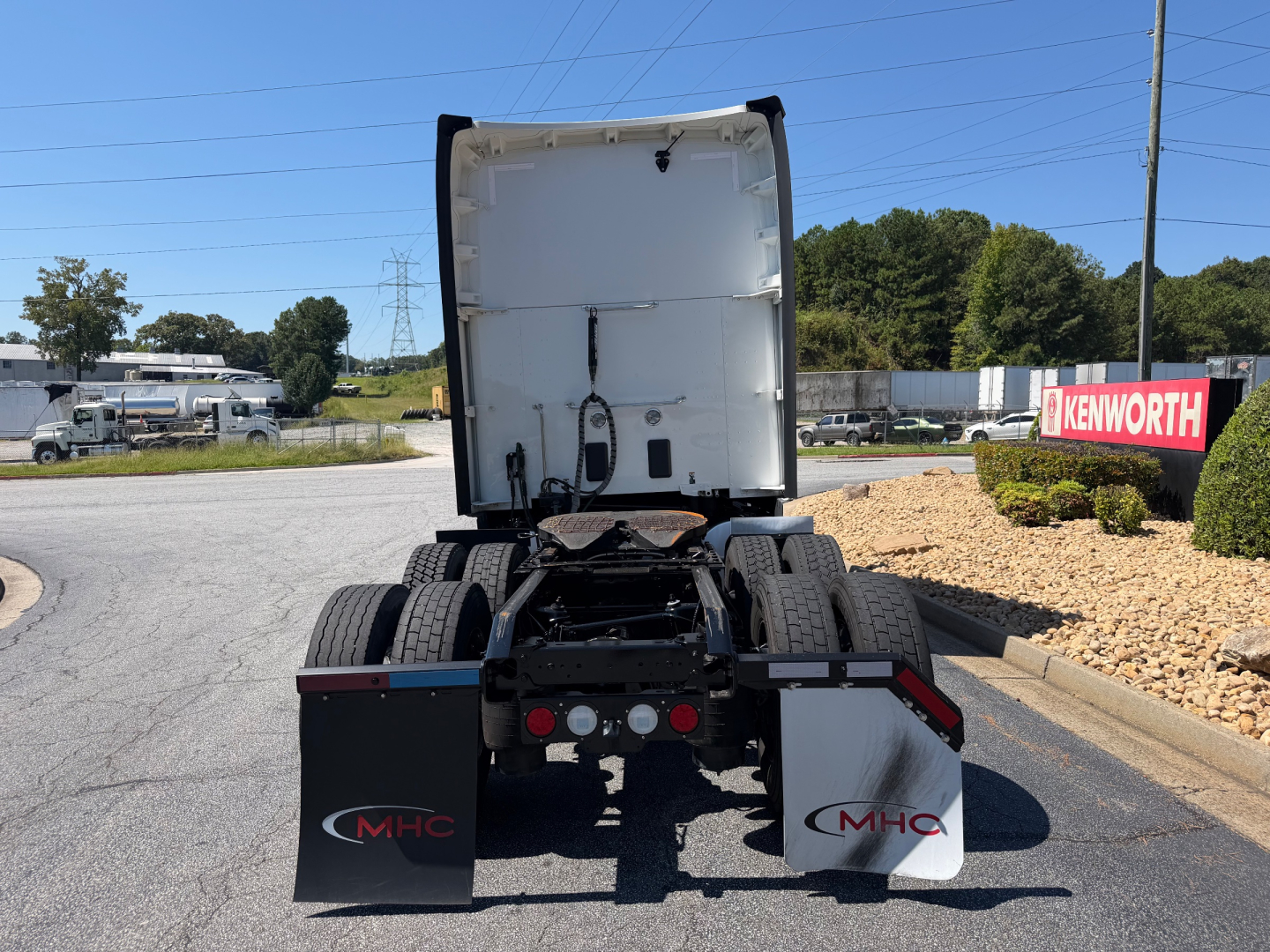 Truck rear view of a Kenworth T680 tractor, fifth wheel area visible, with MHC mud flaps showing MHC logo, and Kenworth sign in background.
