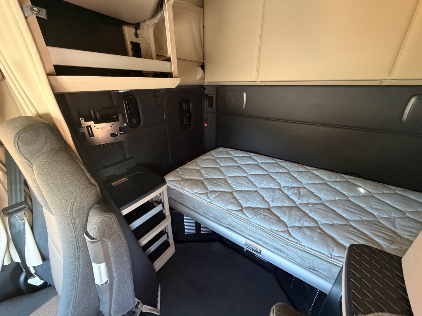 Kenworth T680 sleeper cab interior showing single bed with mattress, storage cubbies, and side panels.