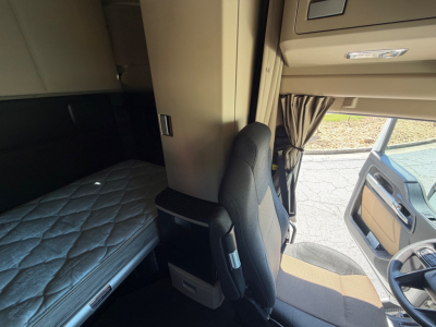 Interior cab of a 2023 Kenworth T680 with sleeper bed, bunk area, and driver seat, right-hand drive view showing entry door and dashboard