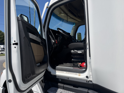 Cabin interior of a 2023 Kenworth T680 truck with driver door open, showing steering wheel and driver's seat.